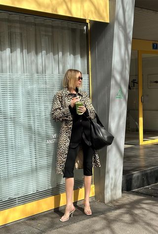 The leopard print coat trend is shown on a woman standing outside wearing TK