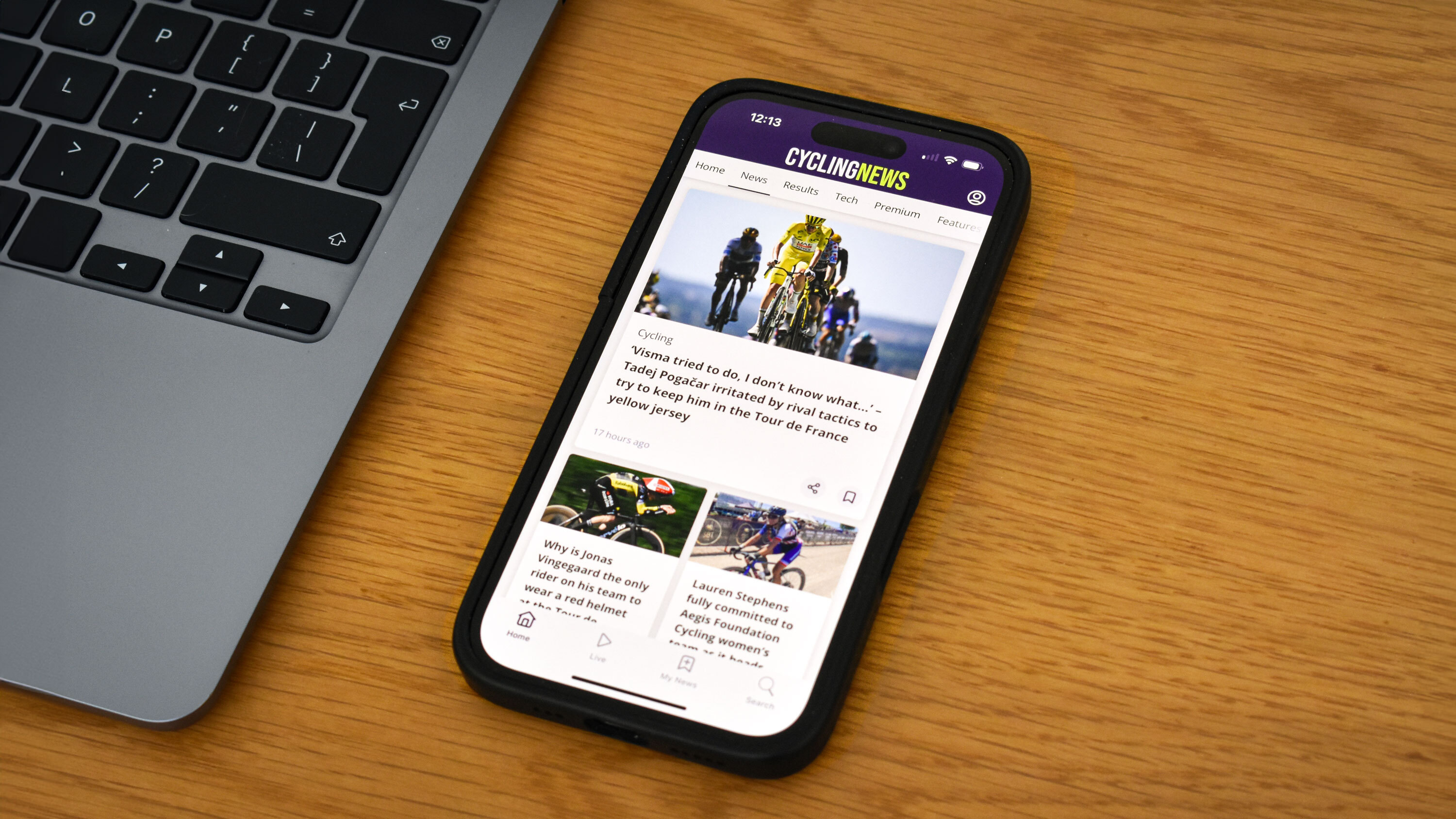 The Cyclingnews app displayed on an iPhone 16 on a table top alongside a laptop.