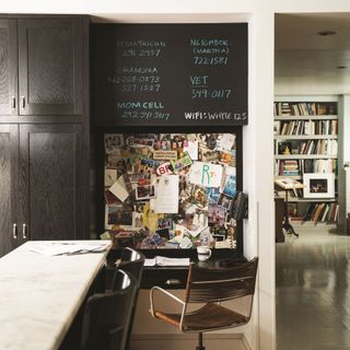 Home office in kitchen with brown cabinetry and chalk paint wall