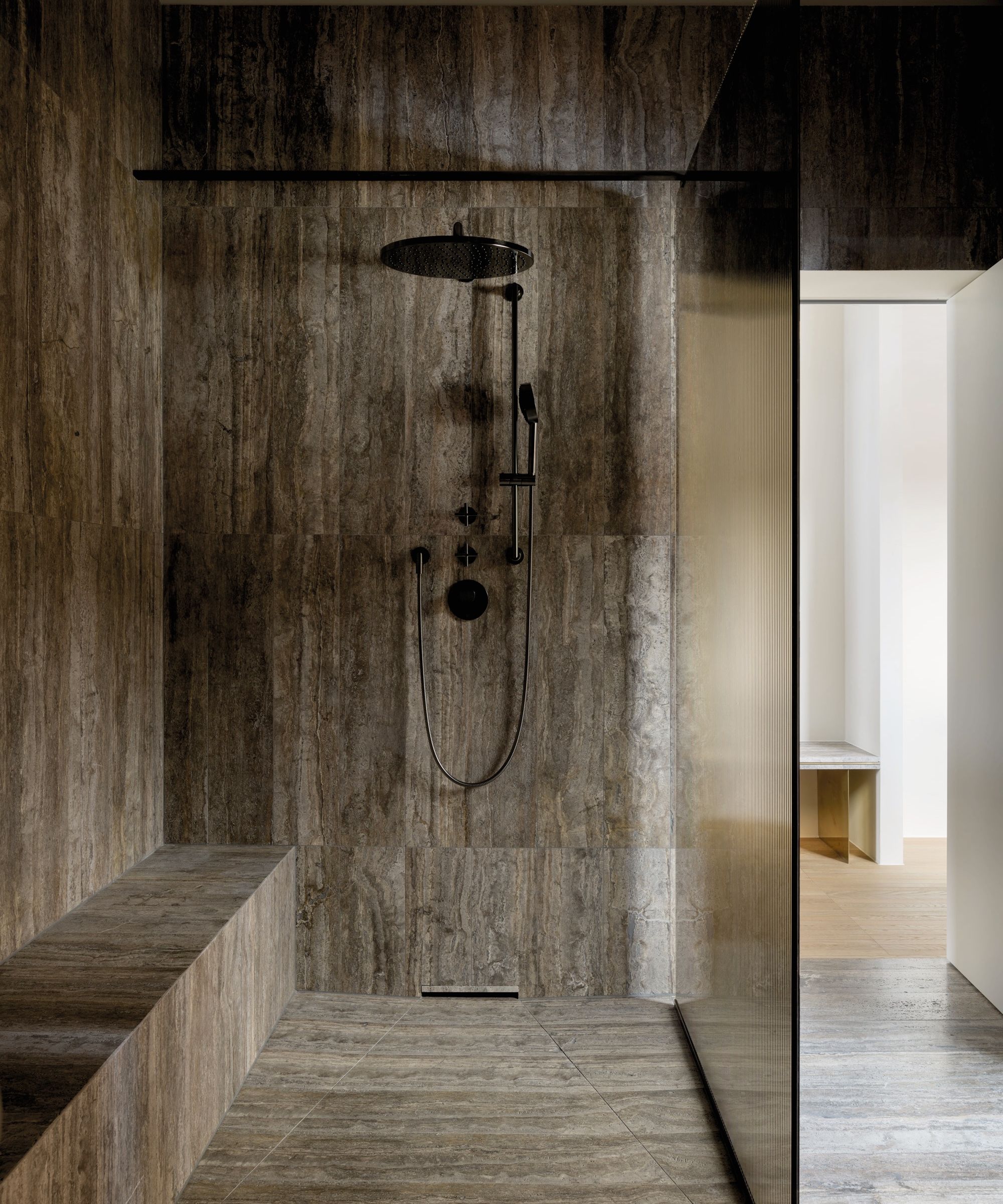 A minimalist walk-in shower with stone-effect tiles, built-in bench seating and matte black fittings for a sleek, spa-inspired space.