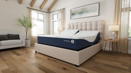 Sleep Number ComfortNext Mattress in a white bedroom with wooden flooring and large windows with sheer curtains.