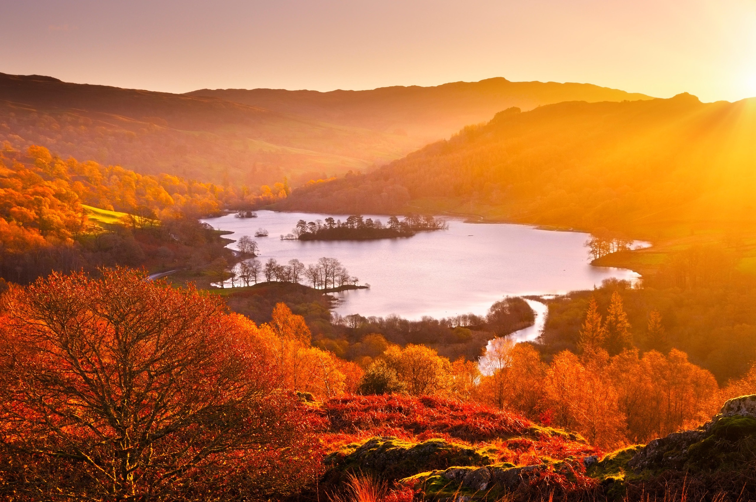 Rydal Water, a lake surrounded by autumn-shaded trees, glows in the late summer sun