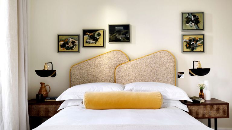 Pandora Taylor yellow shapely headboard with artwork on the walls and yellow bolster cushion 