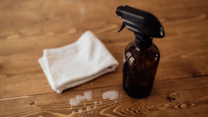 Homemade cleaning spray recipe. Wooden table with cleaning bottle and cloth.