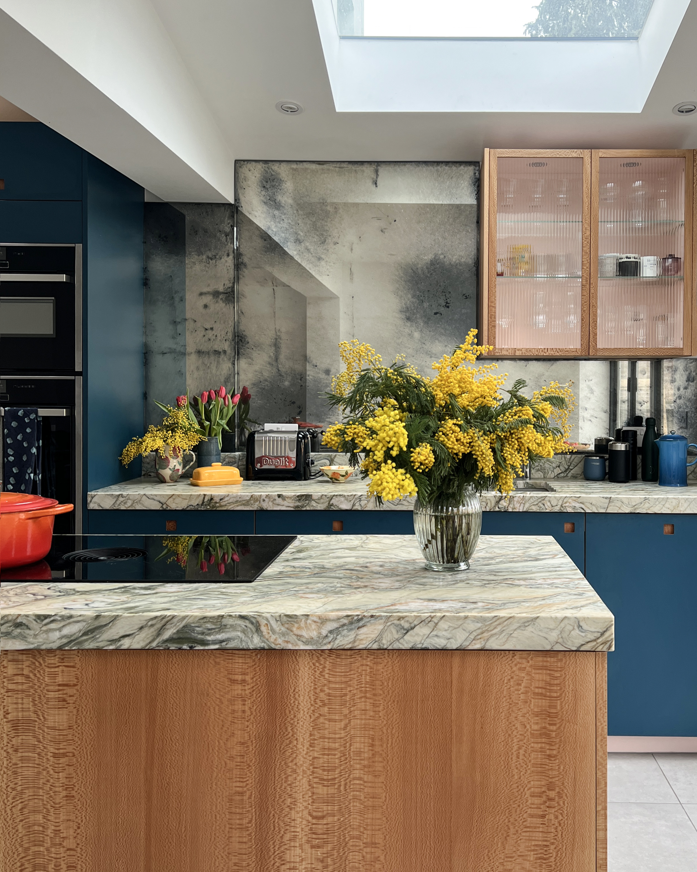 A modern blue kitchen with an antique effect mirrored backsplash.