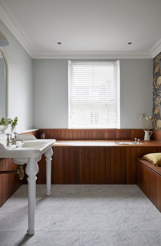 A bathroom with wooden bathtub and large slabs of floor tiles
