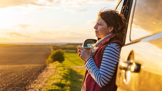 Woman holding cup of coffee standing outside a van looking out across a view