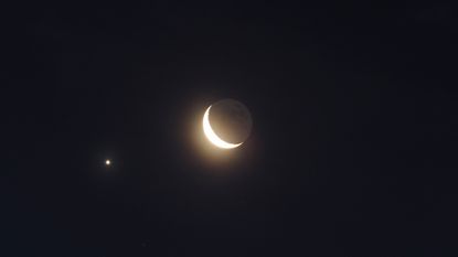 A crescent moon is seen with two small bright stars in the night sky.