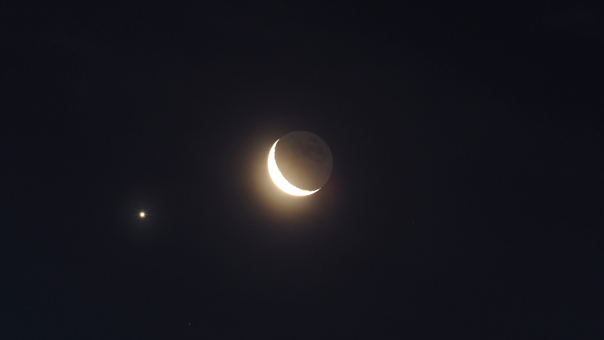 A crescent moon is seen with two small bright stars in the night sky.