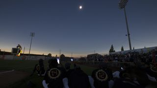 crowds and players gather below to watch the moon eclipse the sun overhead. 