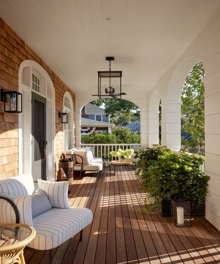 Front porch with arched doorways, wood decking, armchairs, flowerbeds and pendant antique light
