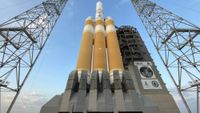 a white and orange rocket stands upright on a launch pad