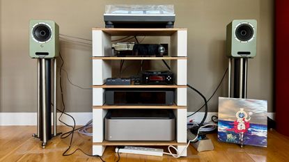 The Fyne Audio Cubitt 5 stereo speaker system, part of a wider hi-fi setup, on a wooden surface.