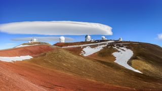 cloud shaped like a flying saucer floating over telescopes on a mountain top