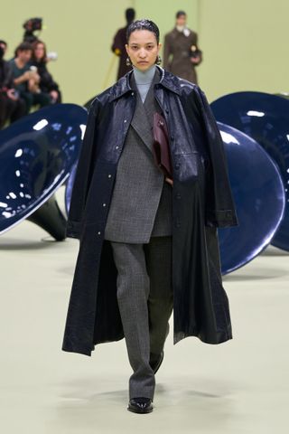 Jil Sander model wearing a navy trench coat over her shoulders with a gray suit and turtleneck.