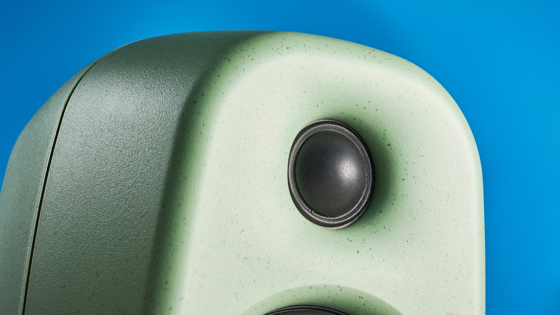 Kanto UKI bookshelf speakers in sage photographed in front of a blue background