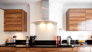 Face on image of contemporary wooden kitchen with stainless steel cooker hood in middle