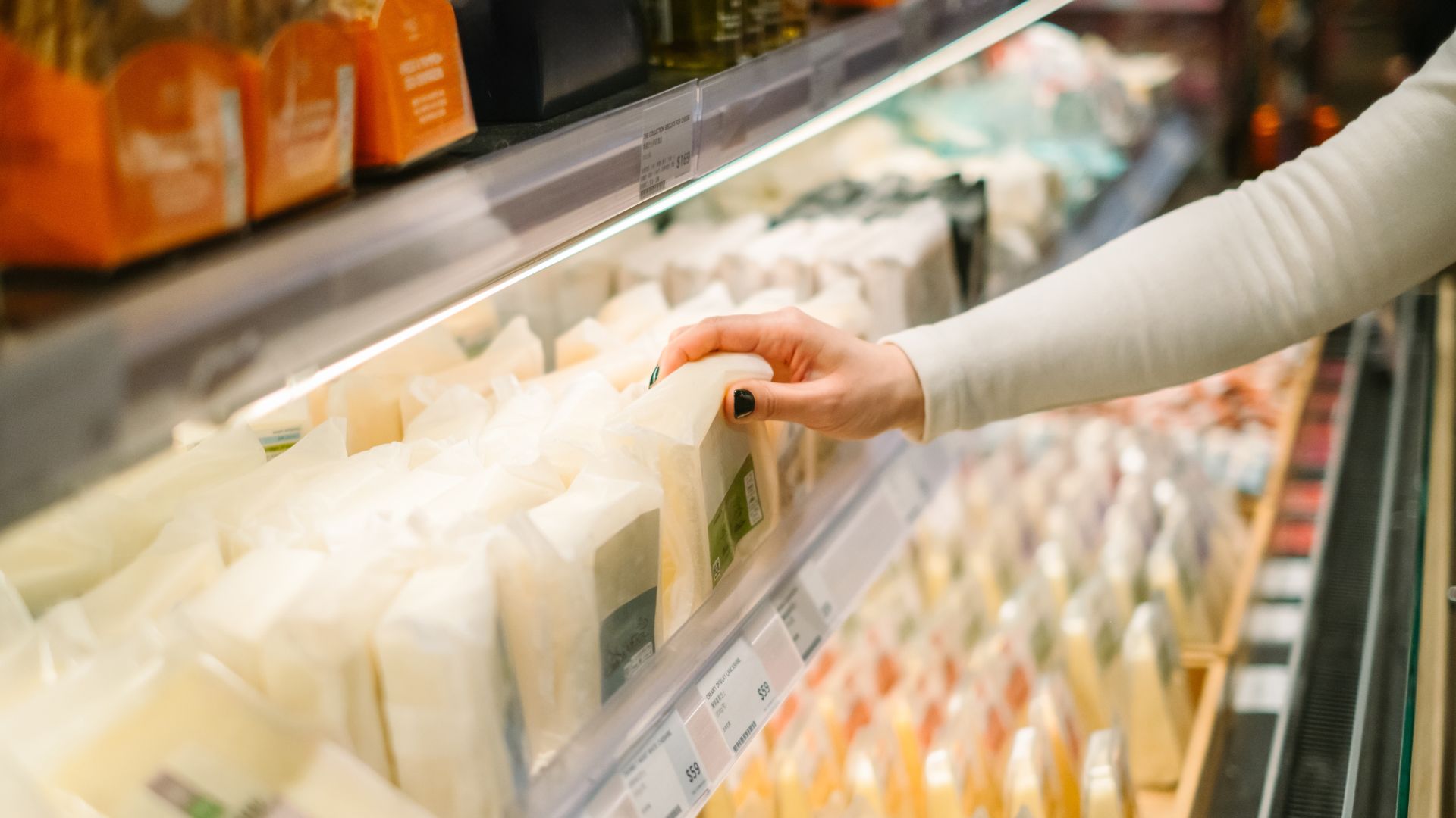 Woman reaching for cheese in a supermarket shelf
