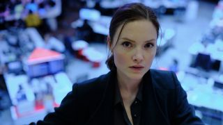 Holliday Grainger wearing a dark jacket and standing in front of desks as Rachel Carey in The Capture season 2.
