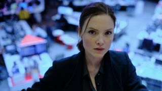 Holliday Grainger wearing a dark jacket and standing in front of desks as Rachel Carey in The Capture