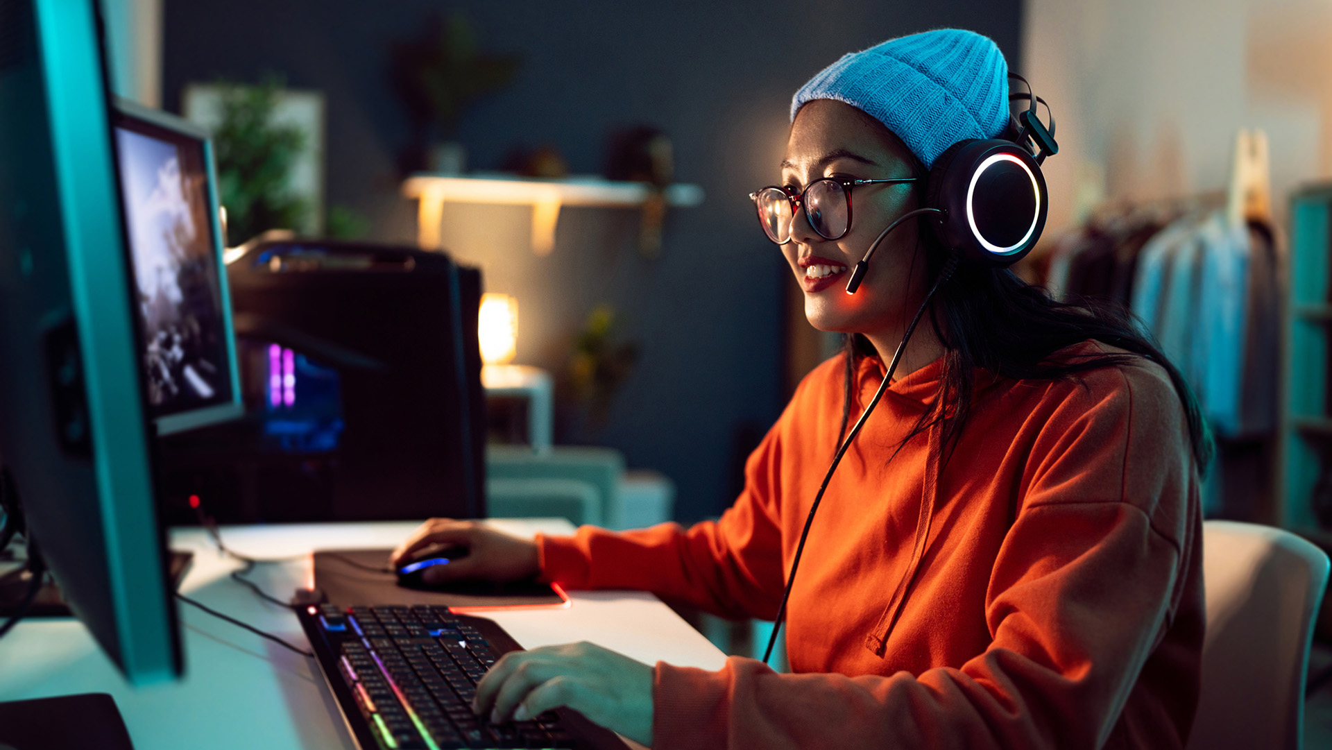 Young female gamer and streamer of Asian ethnicity, playing FPS video games on the computer in her LED-lit room