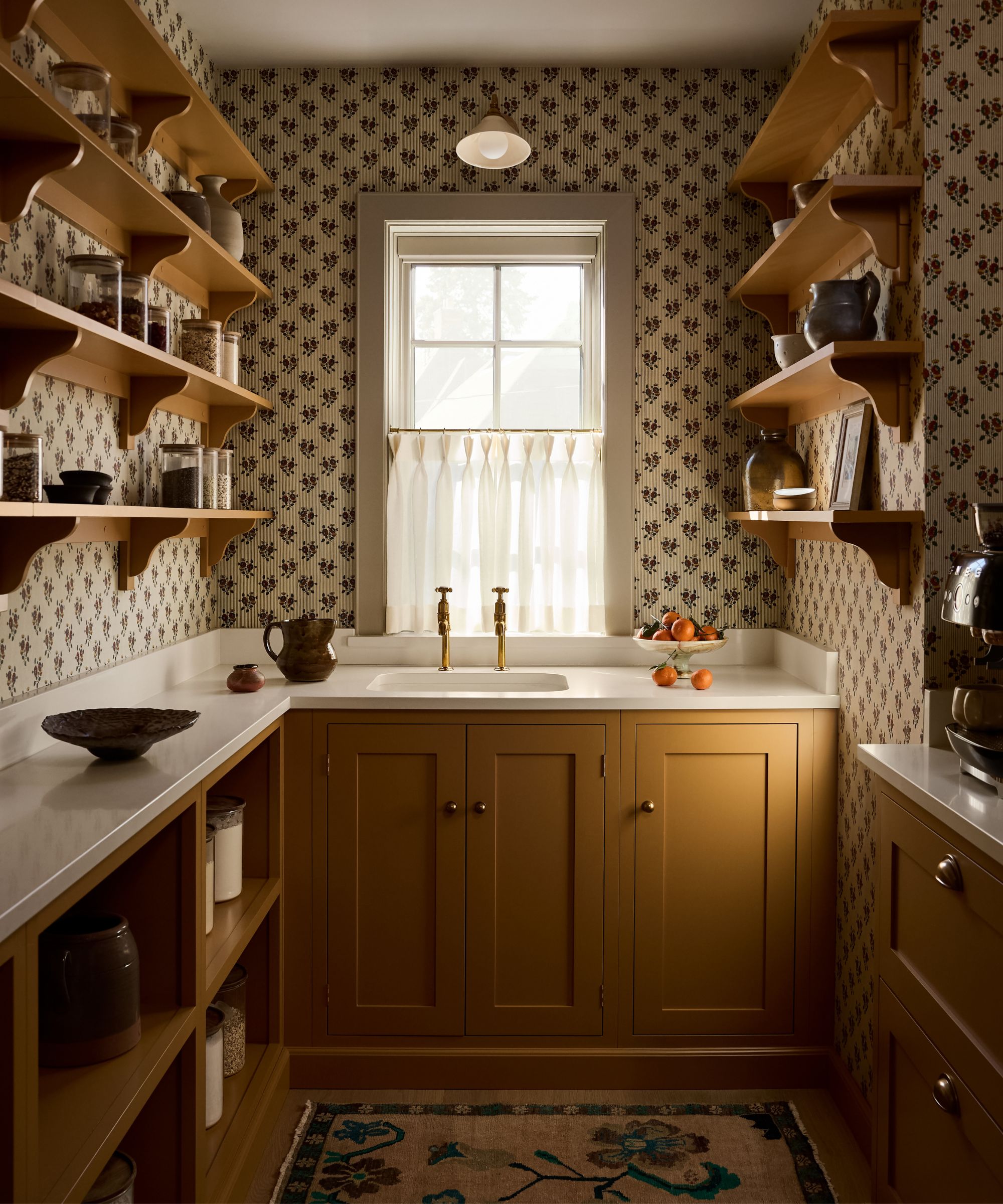 a pantry wrapped in floral wallpaper with ochre yellow cabinetry and open shelving