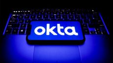 Okta logo and branding pictured on a smartphone screen placed on top of a laptop keyboard.