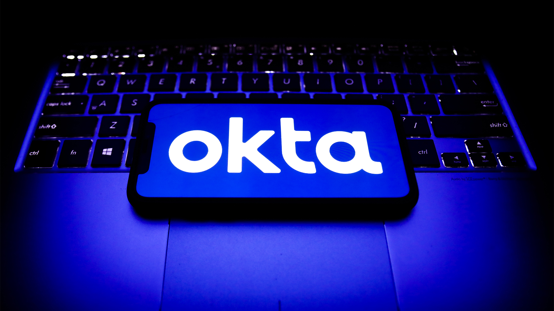 Okta logo and branding pictured on a smartphone screen placed on top of a laptop keyboard.
