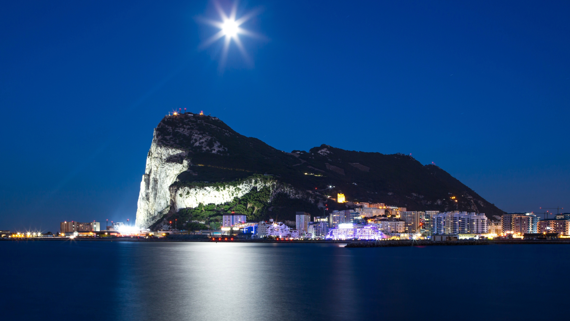 The rock of Gibraltar lights up with nearby city lights during the evening