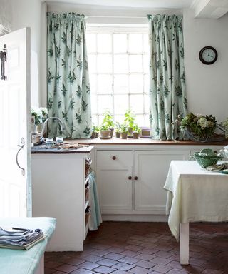 Picture of a kitchen with English country style theme, including floral curtains and tiled floor.
