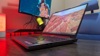 A Lenovo Legion 5i (Gen 9) gaming laptop on a desk with a red backlight, seen at an angle to show the open display, RGB-lit keyboard, and left ports.