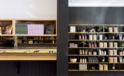 A counter with a selection of macarons and sweets, next to a shelving unit with packaged goods and plants