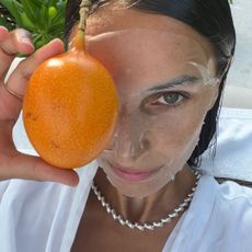 A woman wearing a face mask and holding fruit over her eye.