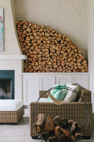 living room with log pile at the side of the fireplace, rattan sofa and footstool