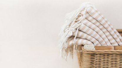 Image shoing half a laundry basket with folded up linens inside, against a white background