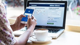 A women holds Apple iPhone 6S with facebook application on the phone screen and on a laptop