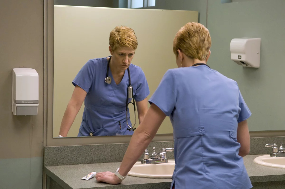 Edie Falco as Jackie Peyton, standing at a public bathroom sink in front of a mirror, in 'Nurse Jackie.'
