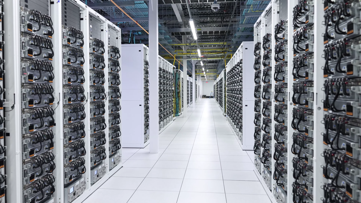 Image of xAI&#039;s Colossus AI supercluster. Two rows of server racks continue into the distance.