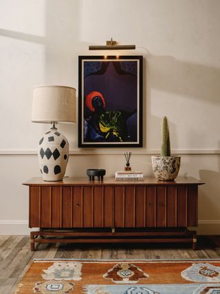 A whimsically decorated passageway features sculptural light, vibrant rugs, and artworks with dark brown tones.