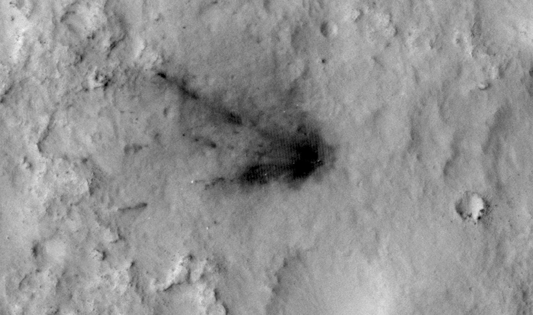 black and white image of the martian surface captured from orbit, showing a large dark smudge where a spacecraft crashed