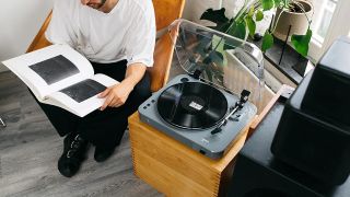 A man reading a book beside at grey and black Lenco L-85 turntable.