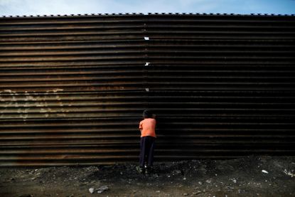 A boy peeking through the U.S.-Mexico border fence.