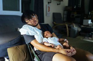 A tired man holding an awake baby at night