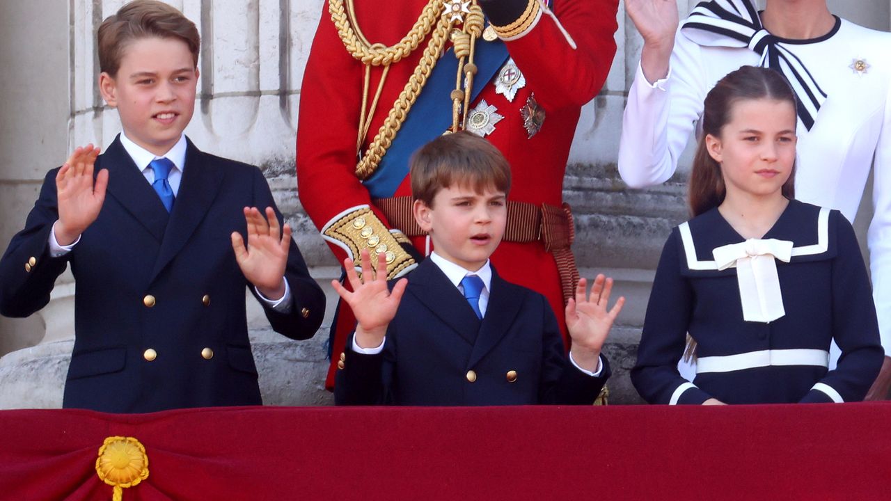 Prince George, Prince Louis and Princess Charlotte wearing navy outfits waving on the balcony of Buckingham Palace with their parents standing behind them