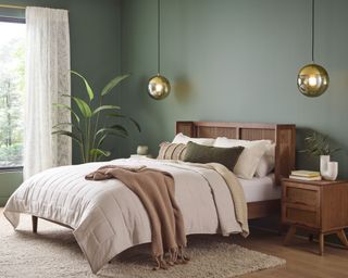 calming bedroom with a sage green wall, round pendant lights, cream bedding and beige carpet