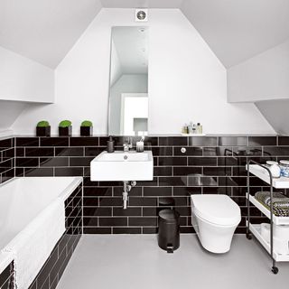 bathroom with black tile and white wall bathtub commode and rectangular mirror