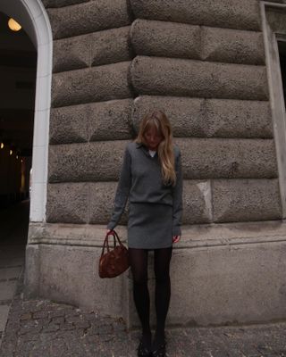 Woman wears a grey mini skirt and sweater.