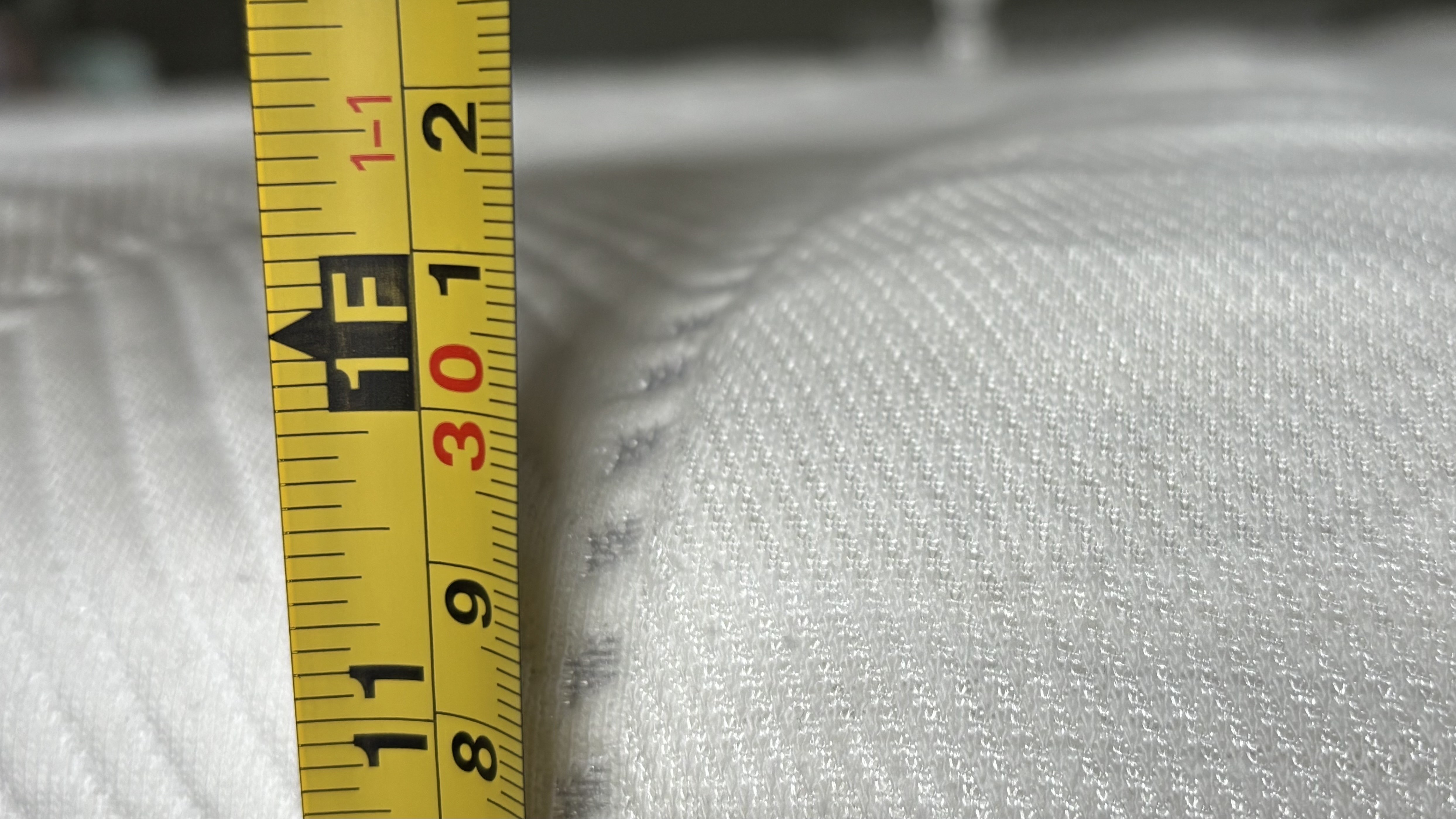 The height of the Leesa Legend Hybrid marked by a yellow measure tape.