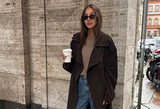 Woman wearing a chocolate brown coat with a light brown sweater and jeans.