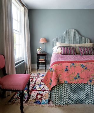 Colorful Bedroom with sage green walls, sash windows, bright bedding and upholstered headboard.